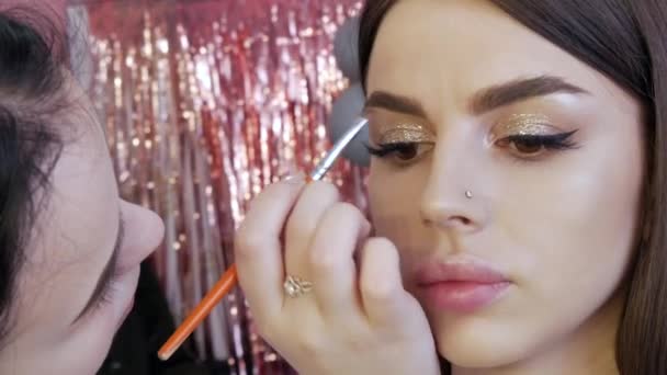 Pensla applicerar skugga på ögonbrynen för att korrigera formen på en vacker ung modell för en kvällssmink för rökiga ögon — Stockvideo