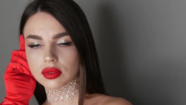 Bella ragazza modello con grandi labbra dipinte con rossetto rosso. Giovane donna in posa con eleganti guanti rossi e brillante trucco serale, guardando la fotocamera — Video Stock