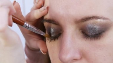 Parlak dumanlı göz makyajlı genç bir kadın modelin güzel anlamlı gözleri. Kendini adamış makyaj fırçası göz alıcı koyu bir bukalemun göz farı sürmektedir.