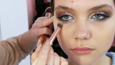 Parlak turkuaz makyajlı mavi gözlü genç bir kızın güzel gözleri. Özel bir fırça, modellerin yüzüne gizleyici temeli uygular.