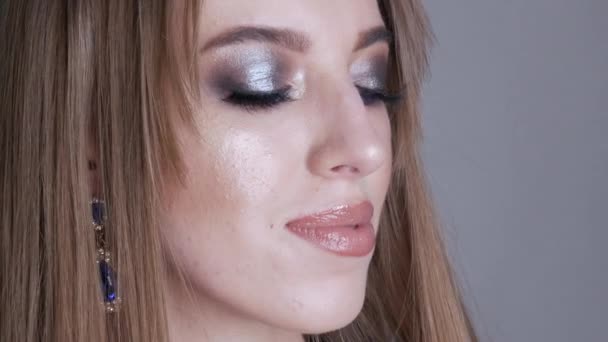 Junges Mädchen Modell mit wunderschönem hellen Abend Make-up mit blauen Schatten mit massiven Ohrringen mit blauen Steinen, die für die Kamera im Studio posieren. Blickt in die Kamera. — Stockvideo