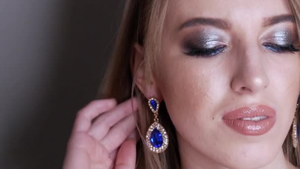 Junges Mädchen Modell mit wunderschönem hellen Abend Make-up mit blauen Schatten mit massiven Ohrringen mit blauen Steinen, die für die Kamera im Studio posieren. Blickt in die Kamera. — Stockvideo
