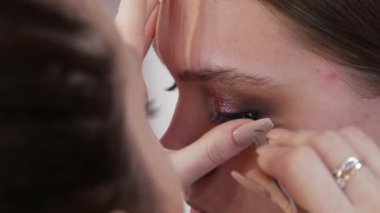 Genç ve güzel bir kız model, profesyonel bir makyaj salonunda parlak bir gece turkuvaz göz makyajına sahte kirpik yapıştırıyor..