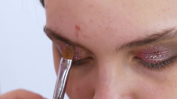 Professionell stylist make-up artist med en borste applicerar skuggor med gnistrar gör ljusa kvällen rökig ögonmakeup på en ung vacker flicka modell med blå ögon — Stockvideo