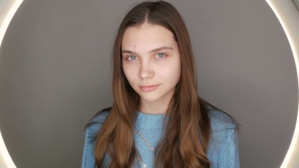Een mooi jong meisje met blauwe ogen in een blauwe trui poseert voor de camera. Model zonder make-up met natuurlijke schoonheid — Stockvideo