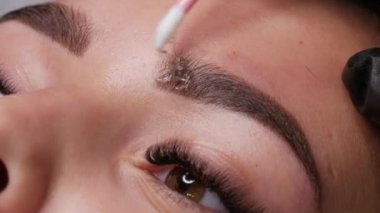 Pamuklu çubukla özel bir jel sürüyorum. Kaşları için kalıcı makyaj yapmış güzel bir genç kız model. Mikro patinaj, kalıcı makyaj dövmesi. Yakın görüş.