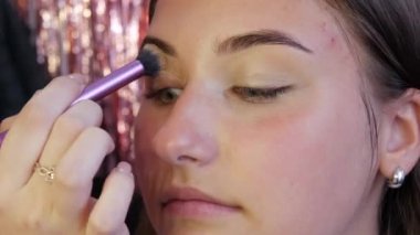 Profesyonel bir makyöz, özel bir fırçayla genç ve güzel bir kızın yüzüne göz makyajı altında bir taban uygular.