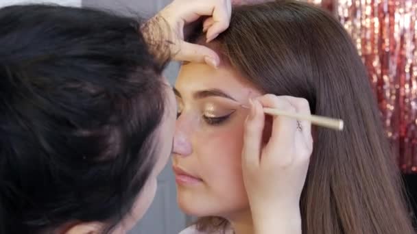Artista stilista ragazza applica una sottile linea di eyeliner viola sul trucco lucido e strass delicati sui modelli occhio, vista da vicino. Trucco di alta moda — Video Stock