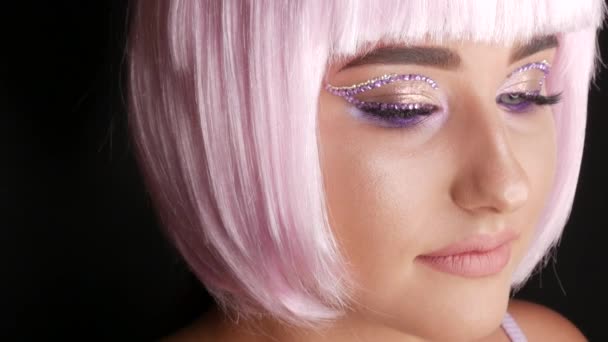 Hermosa joven modelo posando en una peluca bob corto rosa, diamantes de imitación en los ojos y maquillaje rosa con estilo, de alta moda. Cara de cerca — Vídeos de Stock