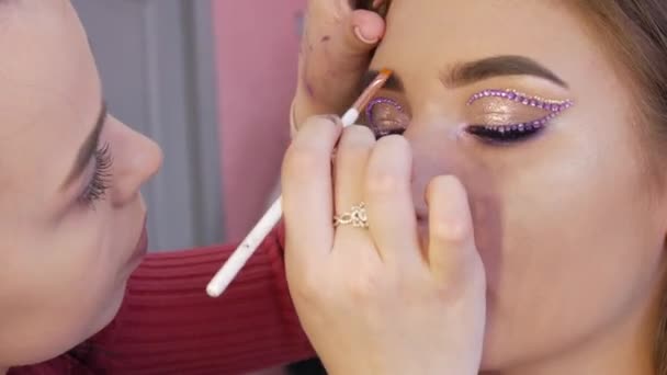 Stylistin Künstler trägt mit einem speziellen Pinsel betont die Form der Augenbrauen auf glänzendes Make-up und zarte Strass auf die Models Auge, Nahsicht. Hohe Mode — Stockvideo