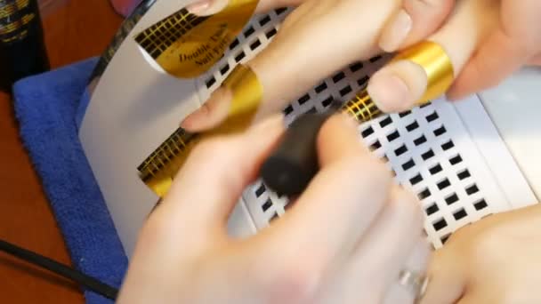 The clear nail polish is applied by a manicurist in a nail salon. Correction and painting of nails close-up view — Stock Video