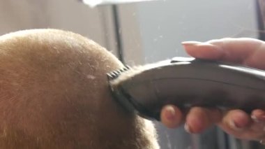 Kadın kuaför, saç kesimi elektrikli tıraş makinesiyle profesyonel kuaför kuaföründe çalışan kızıl saçlı bir müşteri.