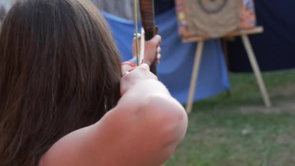 Femme archer avec des pousses de cheveux longs à partir d'un arc avec des flèches sur une cible, vue du dos — Video