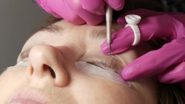 Adult woman face on modern eyelash lamination procedure in a professional beauty salon. The master applies special glue before the eyelash curling procedure in pink rubber gloves close up — Stock Video