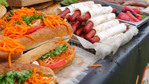Een toonbank met veel worstjes in een pitabrood naast een rij hotdogs en broodjes met sla, wortelen, worst, saus, op een street food festival, ongezond fastfood — Stockvideo