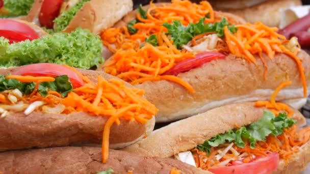 A row of hot dogs and sandwiches with lettuce, carrot, sausage, sauce, at the street food festival, junk fast food — Stock Video