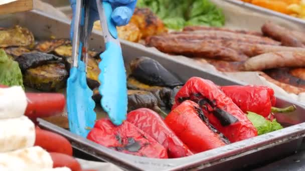 特殊的厨房火钳在茄子和香肠旁边的烤架上放着炸红辣椒，准备在街头食品节的柜台上出售 — 图库视频影像