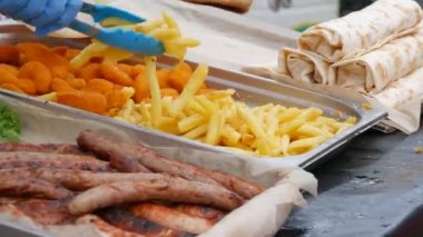 Özel mutfak maşası, sokak yemeği festivalinin tezgahında satılık sosis ve nuggetların yanında patates kızartması toplar.