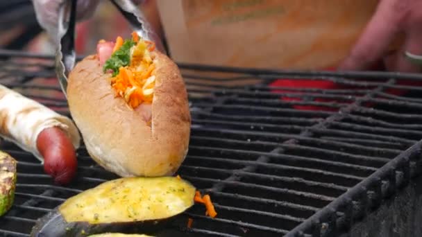 Kokki valmistelee grillattua hot dogia, pitamakkaraa ja paistettua kesäkurpitsaa grillikaupassa, katuruokafestivaali — kuvapankkivideo