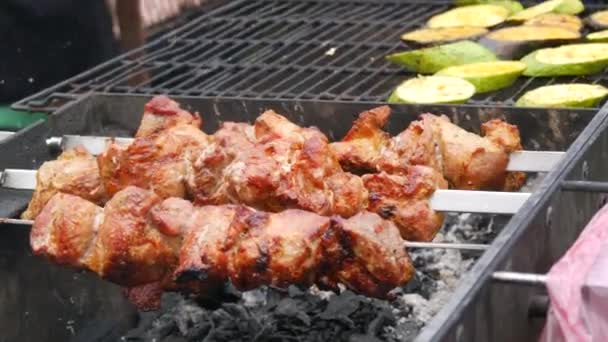 Enormi pezzi di carne alla griglia o kebab che girano accanto alle zucchine sul fuoco della griglia durante un picnic in natura — Video Stock