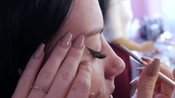 Girl stylist kunstenaar brengt een dunne lijn van zwarte eyeliner op glanzende make-ups in gouden tinten op de modellen oog, close-up bekijken. Mooie stijlvolle avond make-up — Stockvideo