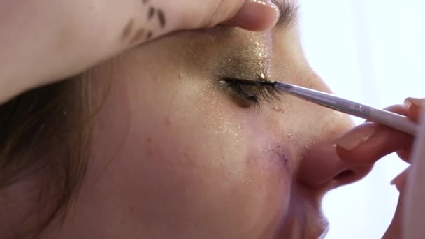 Profesionální vizážista make-up dělá večerní make-up na krásné dívčí modelky. Aplikuje speciální tenkou černou oční linku na víčko — Stock video