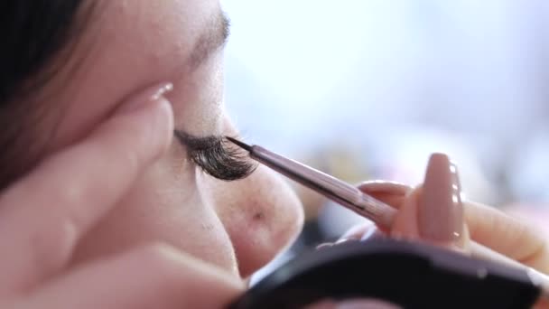 Stylistka dziewczyna stosuje cienką linię czarny eyeliner na błyszczące makijaże w odcieniach złota na modele oczu, widok z bliska. Piękny stylowy makijaż wieczorem — Wideo stockowe