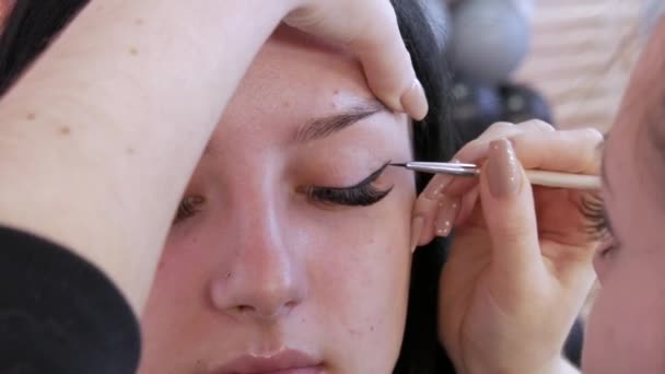 Girl stylist kunstenaar brengt een dunne lijn van zwarte eyeliner op glanzende make-ups in gouden tinten op de modellen oog, close-up bekijken. Mooie stijlvolle avond make-up — Stockvideo