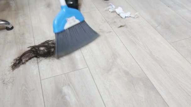 Broom dan sendok menyapu banyak rambut manusia dari lantai di sebuah toko cukur setelah memotong — Stok Video