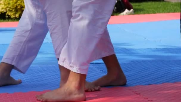 Ноги спортсменов в кимоно, занимающихся уличной борьбой на специальных карематах. Массовая подготовка спортсменов-каратистов — стоковое видео