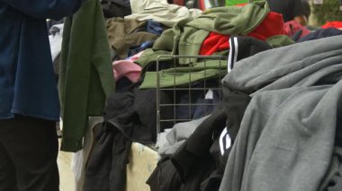 İkinci el kıyafetlerin farklı renklerde karışımına el yordamıyla bakan bir adam. Sürdürülebilir alışveriş alışkanlıkları ve minimalist yaşam tarzının sembolü.