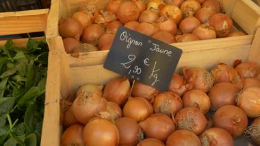 Fransa 'daki Provencal çiftçi pazarında ahşap bir sandıkta sergilenen taze sarı soğanlar. Fiyat etiketi Fransızca yazılmış ve özgün bir yerel dokunuş eklenmiş.