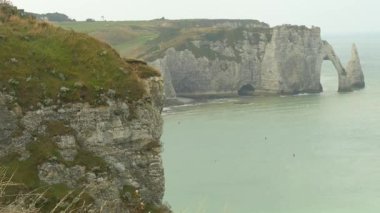 Etretat kayalıkları ve Normandiya 'nın doğal kemeriyle sahilin manzarası. Suyun üzerinde dramatik kireç taşı oluşumları. Popüler turizm alanının üzerindeki yeşil tepeler ve Atlantik kıyısının sembolü.