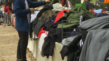 Açık hava pazarında ikinci el kıyafetlere bakan bir adam. Çevre dostu yaşam tarzı, bilinçli tüketim ve dairesel ekonomi kavramını temsil eder.