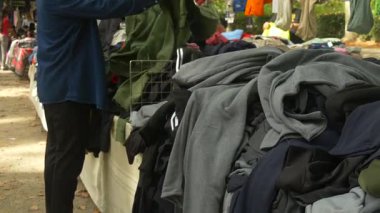 İnsanlar ikinci el kıyafetlerin arasından el yordamıyla ararlar. Dikkatli alışverişi temsil eder, atıkları azaltır ve sürdürülebilir yaşamı destekler