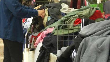 Bir adamın ikinci el pazarında kullanılmış kıyafetleri karıştırdığı gerçek bir an. Günlük basitliği ve çevre dostu yaşamla bağlantıyı yakalar.