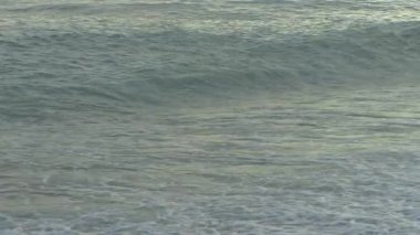 Yumuşak okyanus dalgalarının akşam ışığında çakıl taşı plajına değdiği huzurlu bir manzara. Rahatlama, farkındalık ve kıyı sükuneti kavramı.