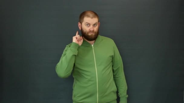 Um homem com barba, indicador, mostra Importante ou Atenção. Ele está vestido com um fato de treino verde. — Vídeo de Stock