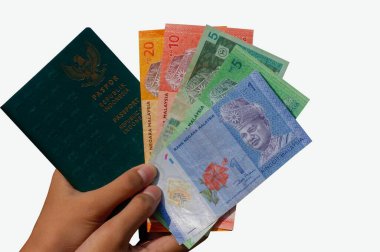 Ellerinde Ringgit Malezya parası ve Endonezya pasaport defteri var. Beyaz arka planda sığ bir odak noktası var. Endonezya 'dan gelen göçmen çalışanlar kavramı