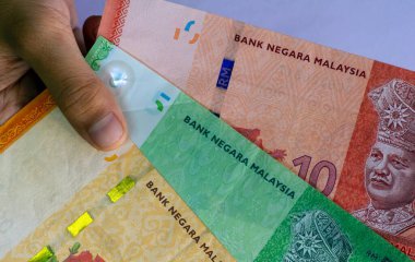 Asyalı çocuğun eli Ringgit Malezya 'nın parasını sığ bir odak noktasında tutuyor.