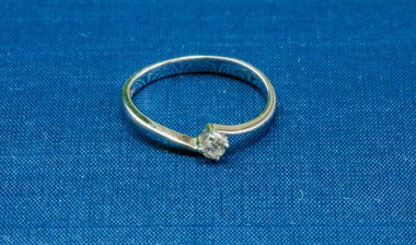 Mavi bir paspasın üzerinde bir mücevher olan beyaz bir altın yüzük.