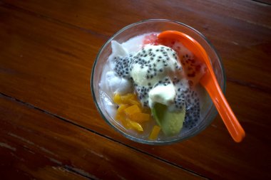 Bir kase Durian kremalı dondurma ve fesleğen tohumları ve tatlı meyvelerle süslenmiş bir portakal kaşığı..