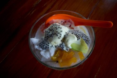 Bir kase Durian kremalı dondurma ve fesleğen tohumları ve tatlı meyvelerle süslenmiş bir portakal kaşığı..