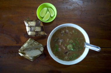 Coto Makassar, ketupatlı sığır eti çorbası ahşap bir masada dilimlenmiş limon Güney Sulawesi, Makassar 'dan geleneksel Endonezya yemekleri..