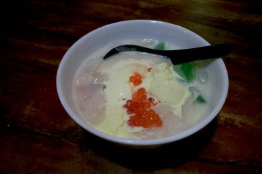 A bowl of creamy ice cream and a black spoon, on a wooden table.