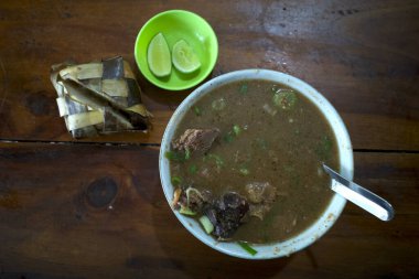 Coto Makassar, ketupatlı sığır eti çorbası ahşap bir masada dilimlenmiş limon Güney Sulawesi, Makassar 'dan geleneksel Endonezya yemekleri..