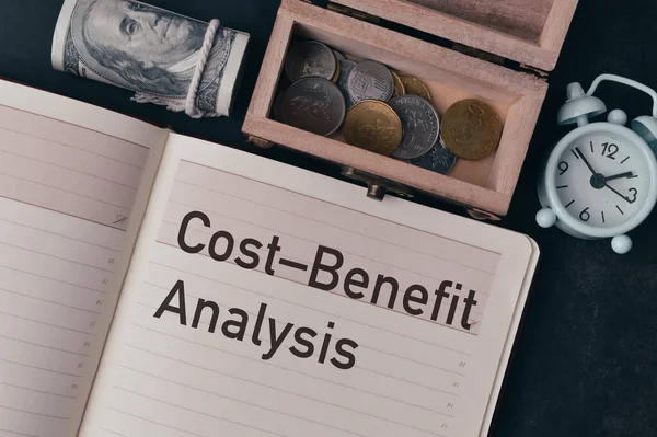 Top view of coins, money banknotes and notebook written with COST BENEFIT ANALYSIS