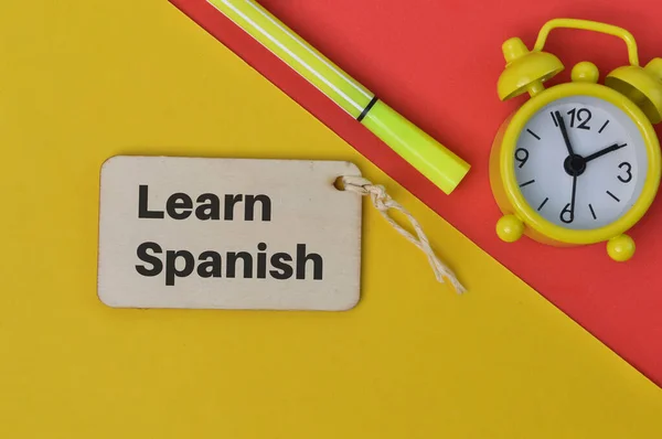Saat, kalem ve tahta etiket LeARN SPANISH ile yazılmış.