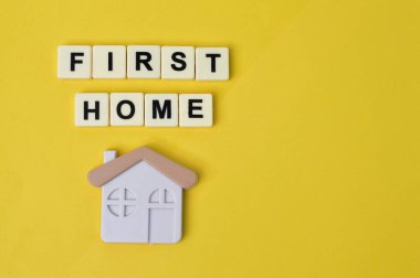 Toy house and square letters with text FIRST HOME.