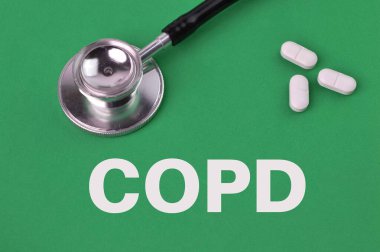 Kronik obstrüktif akciğer hastalığı anlamına gelen COPD ile yazılmış yeşil arka plan üzerinde ilaç kapsülleri ve stetoskop.
